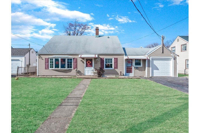 View of front facade with driveway, a front yard, a shingled roof, a garage, and a chimney