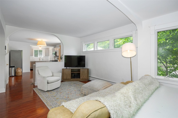 Living room with arched walkways, dark wood-style floors, and a baseboard radiator
