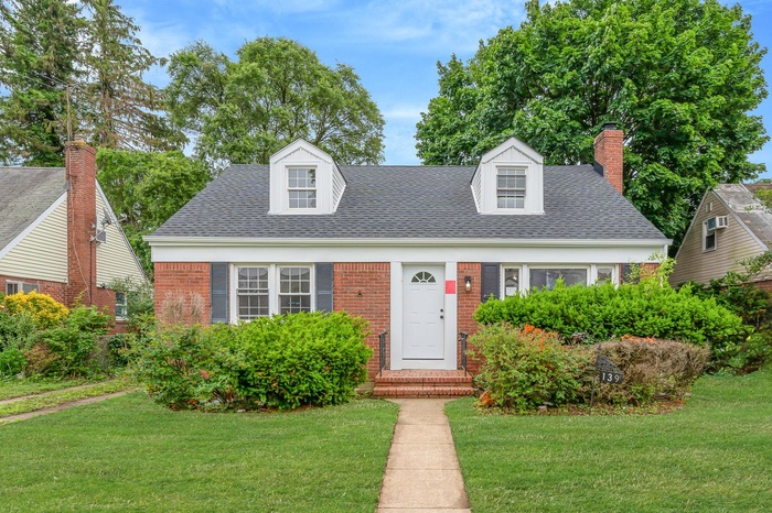 New england style home featuring a front yard, a shingled roof, brick siding, and a chimney