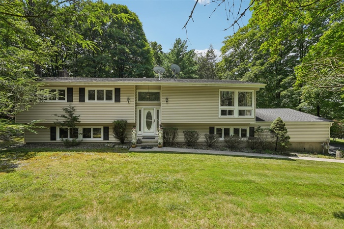 Raised ranch featuring a front lawn, entry steps, and view of wooded area