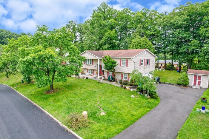 Bi-level home featuring a shed, a front yard, asphalt driveway, and view of scattered trees