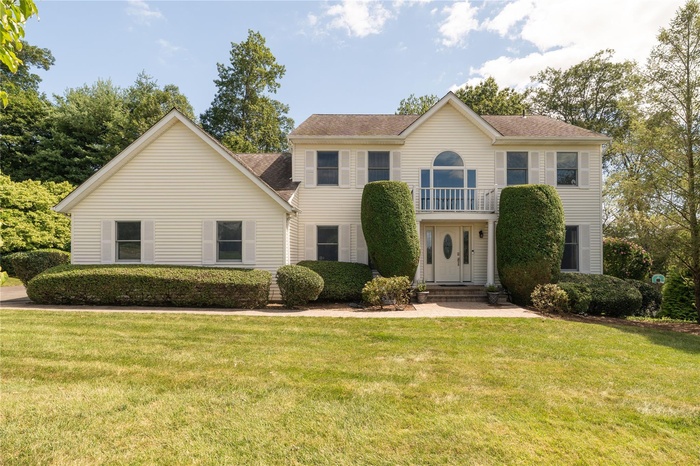Colonial house with a balcony, a front yard, and a shingled roof