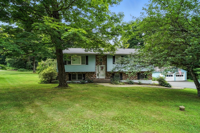 Bi-level home featuring a front yard, asphalt driveway, brick siding, a garage, and a shingled roof
