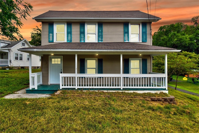 View of front facade featuring covered porch and a lawn