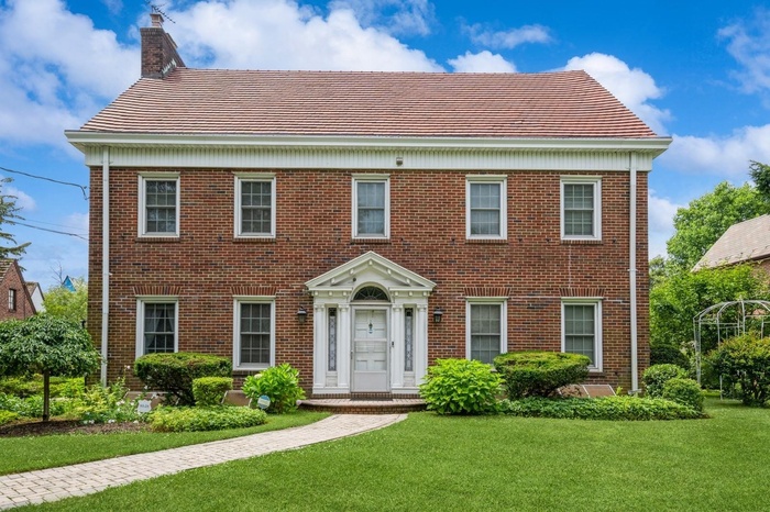View of front facade featuring a front yard, brick siding, and a chimney