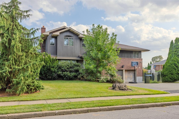 View of front facade with brick siding, an attached garage, driveway, a chimney, and a front lawn