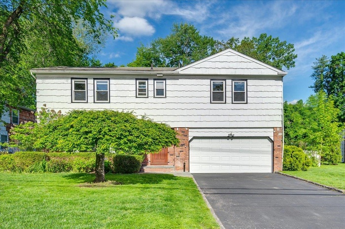 View of front of home with brick siding, a garage, driveway, and a front lawn