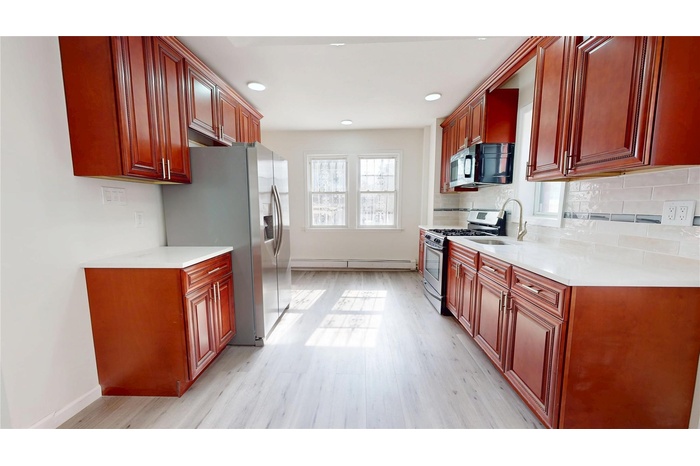 Kitchen featuring appliances with stainless steel finishes, light countertops, light wood-style flooring, and decorative backsplash