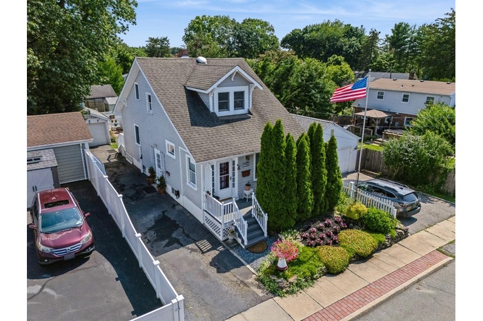 View of front facade with roof with shingles, an outbuilding, a fenced backyard, driveway, and view of wooded area