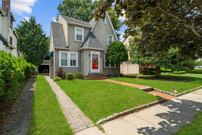 Tudor-style house featuring roof with shingles, stucco siding, a front yard, and entry steps