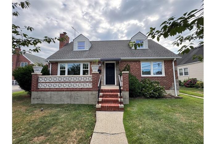 Cape cod house with brick siding, a front lawn, roof with shingles, and a chimney