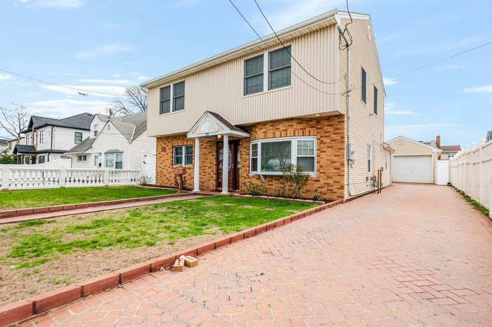 View of front of home with an outdoor structure, a detached garage, decorative driveway, brick siding, and fence