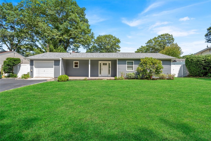 Ranch-style home with an attached garage, asphalt driveway, roof with shingles, and a porch