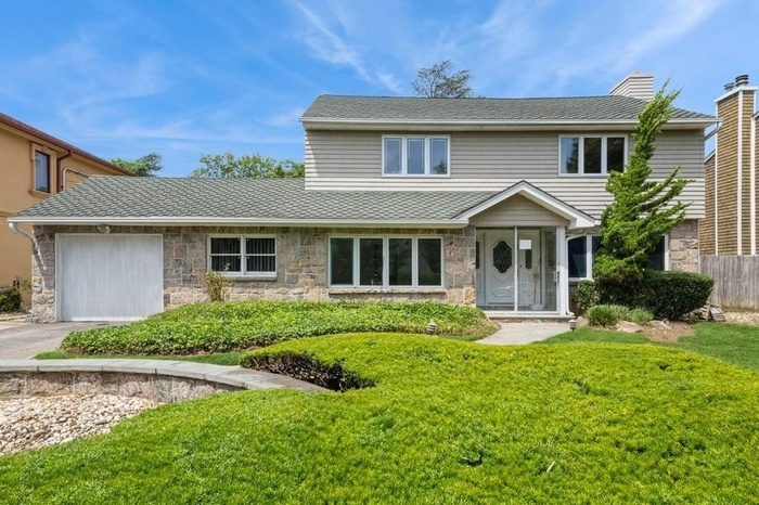 Traditional home featuring stone siding, a garage, driveway, and a chimney