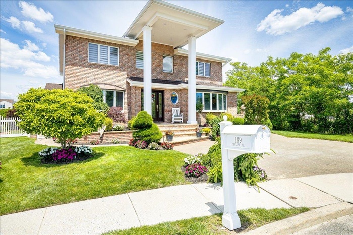Greek revival inspired property with brick siding, driveway, and a front lawn