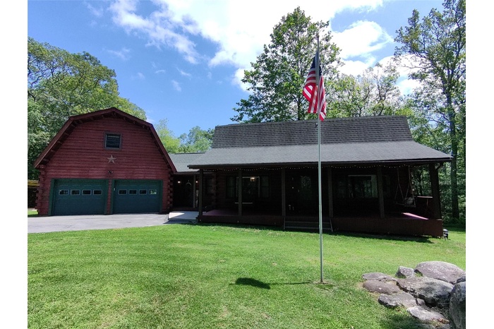 View of front of house with a front lawn, driveway, log siding, and roof with shingles