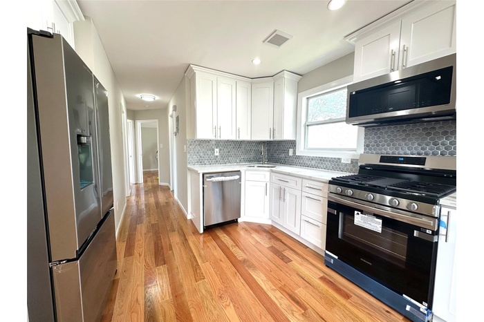Kitchen featuring appliances with stainless steel finishes, white cabinetry, light wood-style floors, decorative backsplash, and recessed lighting