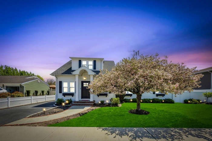 View of front facade with fence, a shingled roof, and a lawn