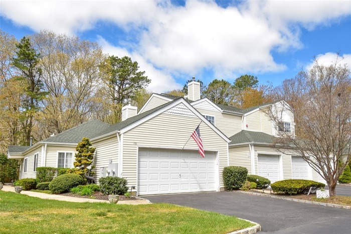 Traditional home featuring a chimney, driveway, a garage, and a shingled roof