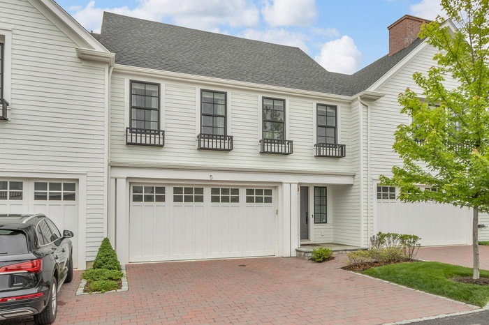 View of front of home featuring decorative driveway, an attached garage, a chimney, and a shingled roof