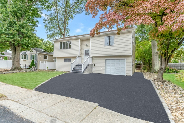 Bi-level home featuring driveway, a front lawn, fence, and an attached garage