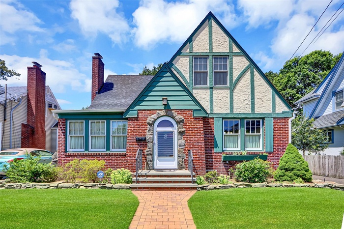 Tudor home with brick siding, a chimney, and stucco siding