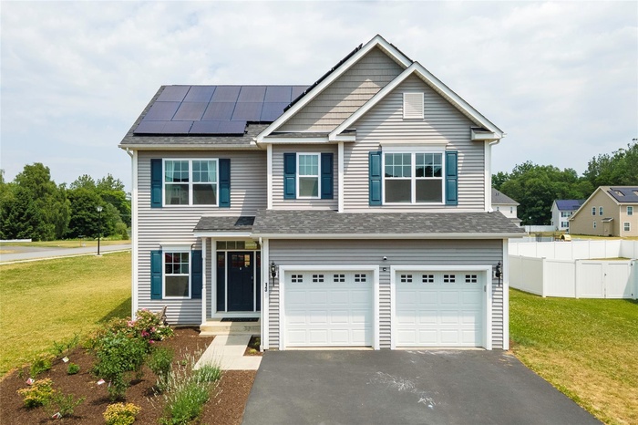 View of front of home featuring a front yard, fence, aphalt driveway, roof mounted solar panels, and a garage