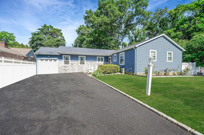 Ranch-style home featuring an attached garage, driveway, and stone siding