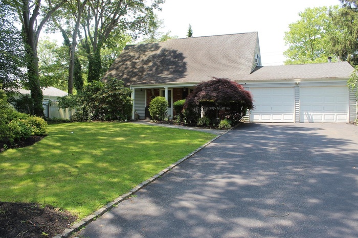 Cape cod home featuring driveway, an attached garage, a front yard, and roof with shingles