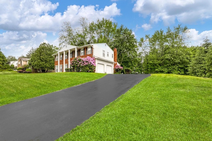 Greek revival house featuring a chimney, driveway, a garage, brick siding, and a front yard