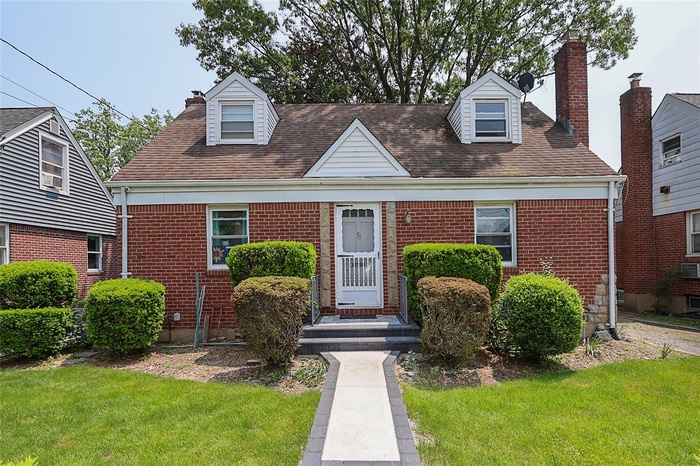 Cape cod-style house featuring a front lawn, brick siding, and a chimney