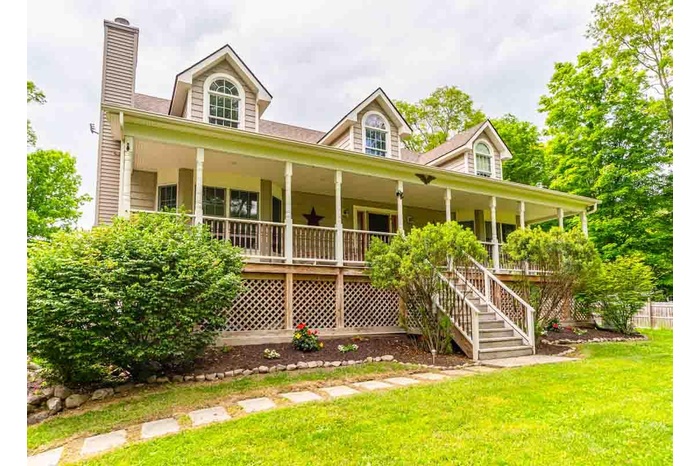 View of front facade featuring covered porch, a chimney, a front lawn, and stairway