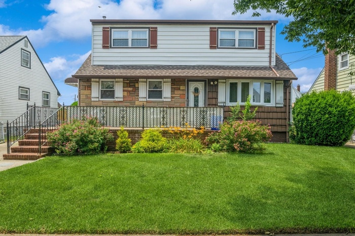 View of front of home with a shingled roof, a front yard, covered porch, and stone siding