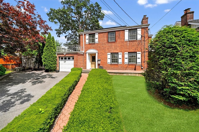 Colonial inspired home with driveway, a chimney, a balcony, brick siding, and a garage