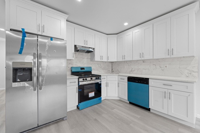 Kitchen featuring appliances with stainless steel finishes, tasteful backsplash, under cabinet range hood, light wood-type flooring, and white cabinet