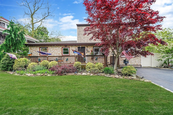 View of front of home featuring stone siding, driveway, a deck, and a front lawn