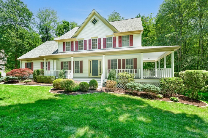View of front facade with covered porch, a shingled roof, and a front lawn
