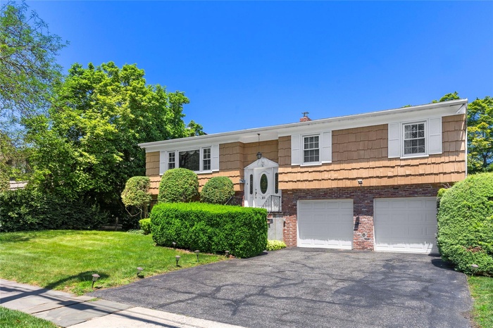Split foyer home featuring brick siding, an attached garage, driveway, and a front yard