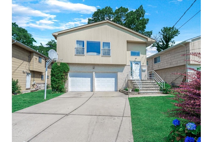 Split level home with brick siding, an attached garage, driveway, and a front lawn