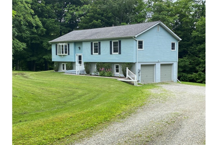 Bi-level home with gravel driveway, an attached garage, and a front yard