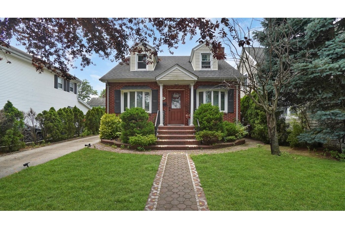 Cape cod-style house featuring a shingled roof, brick siding, and a front lawn