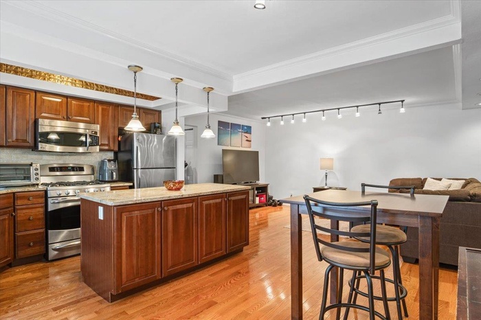 Kitchen featuring stainless steel appliances, a kitchen island, open floor plan, light wood-style floors, and crown molding