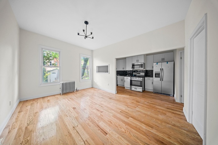 Kitchen with appliances with stainless steel finishes, radiator heating unit, gray cabinetry, light wood-style floors, and a chandelier