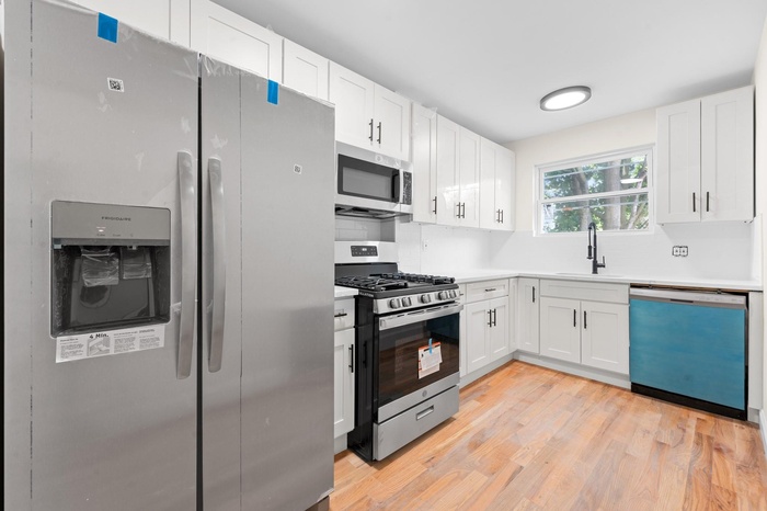 Kitchen featuring appliances with stainless steel finishes, white cabinetry, light wood-type flooring, and light countertops