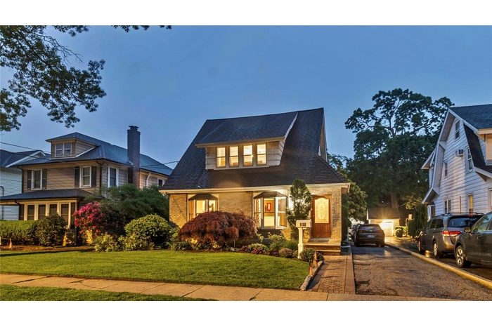 View of front of house featuring brick siding, asphalt driveway, a front yard, and roof with shingles