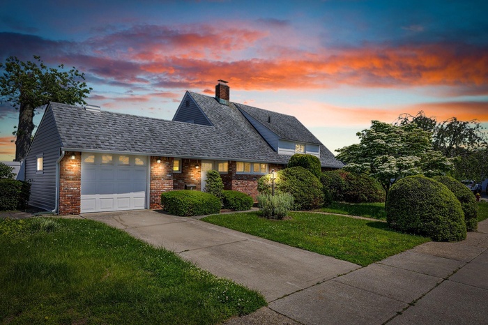 View of front of home featuring brick siding, driveway, a lawn, an attached garage, and a chimney