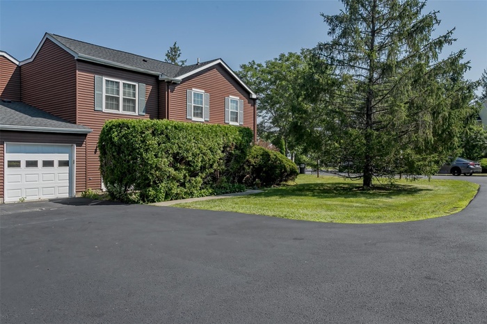 View of front facade with driveway, roof with shingles, an attached garage, and a front lawn