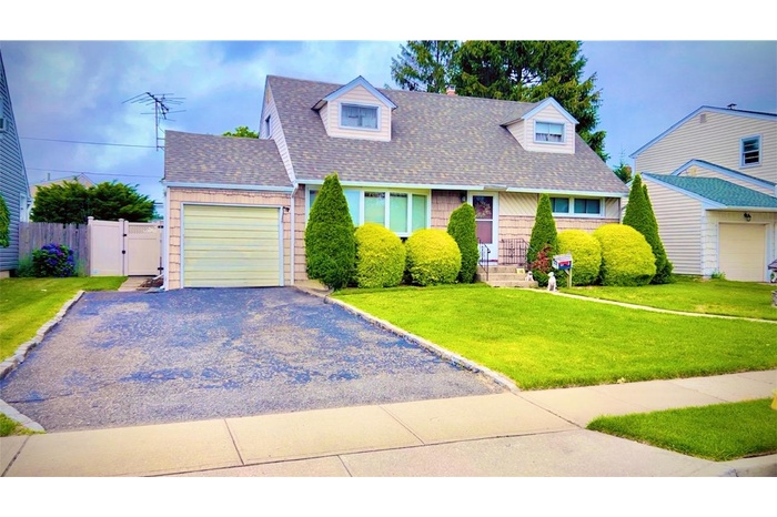 Cape cod house with a garage, a shingled roof, a gate, and gravel driveway