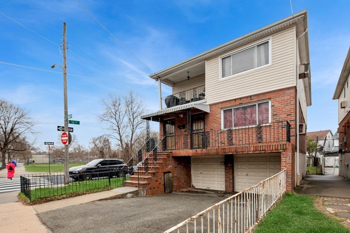Rear view of house featuring driveway, fence, brick siding, a balcony, and a garage