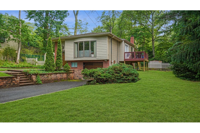View of front of house featuring a chimney, an attached garage, driveway, a deck, and brick siding